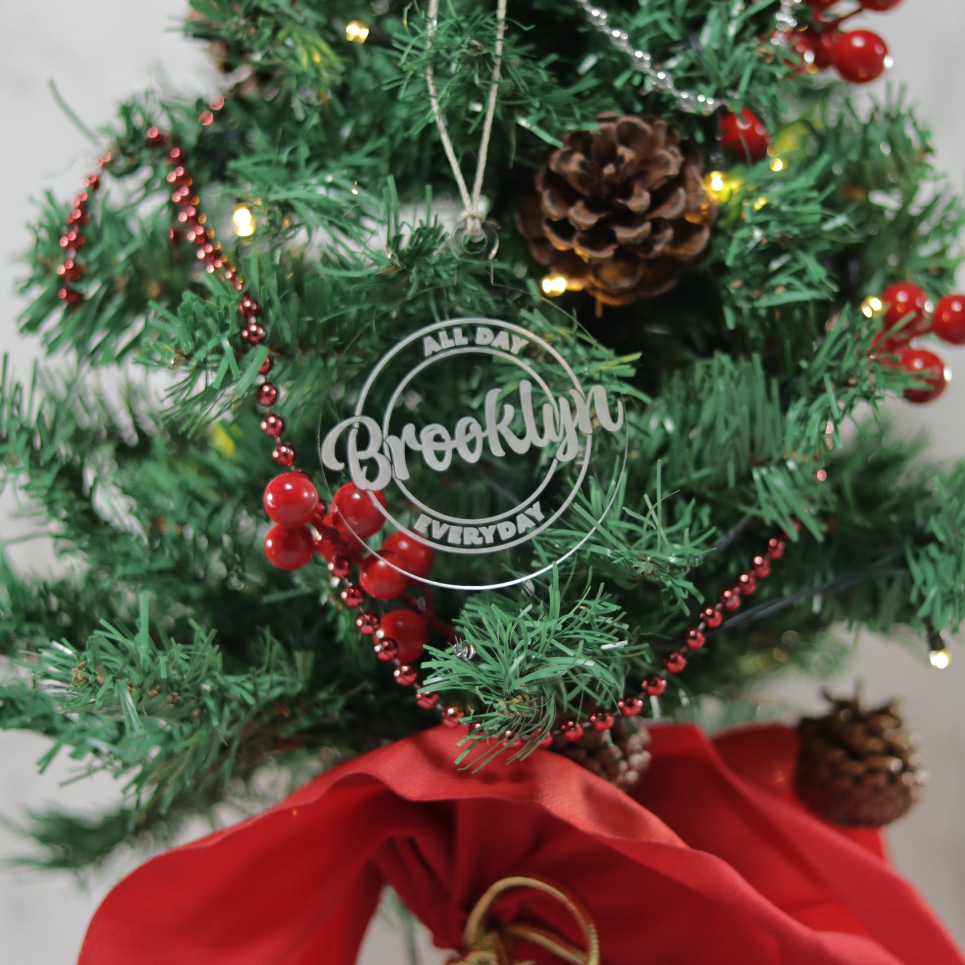 Round clear acrylic ornament on a mini Christmas tree. The words Brooklyn all day everyday is etched in the ornament.